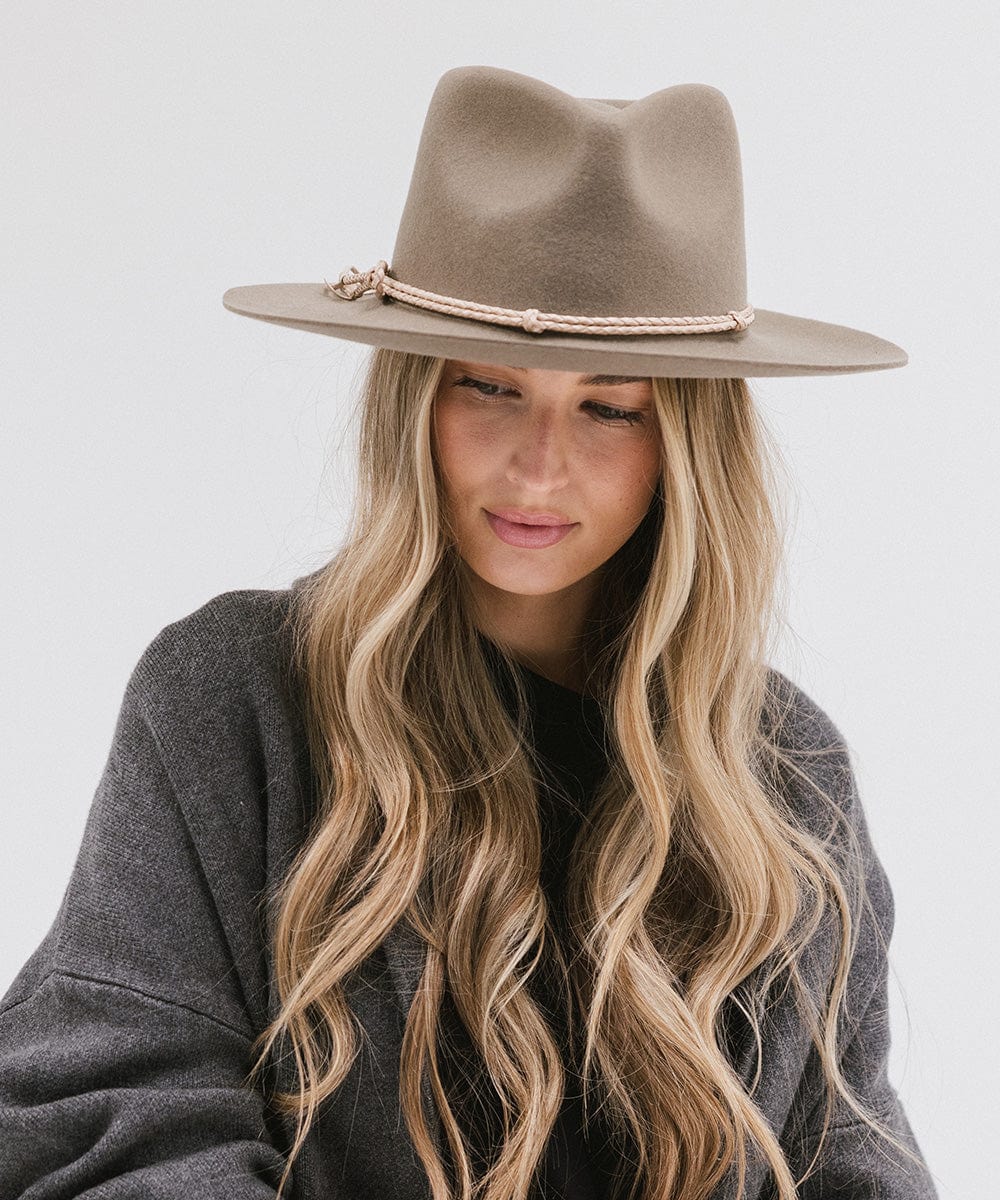 Woman wearing cowboy hat with a beige lasso braided hat band and a grey sweater against a plain background #color_cream