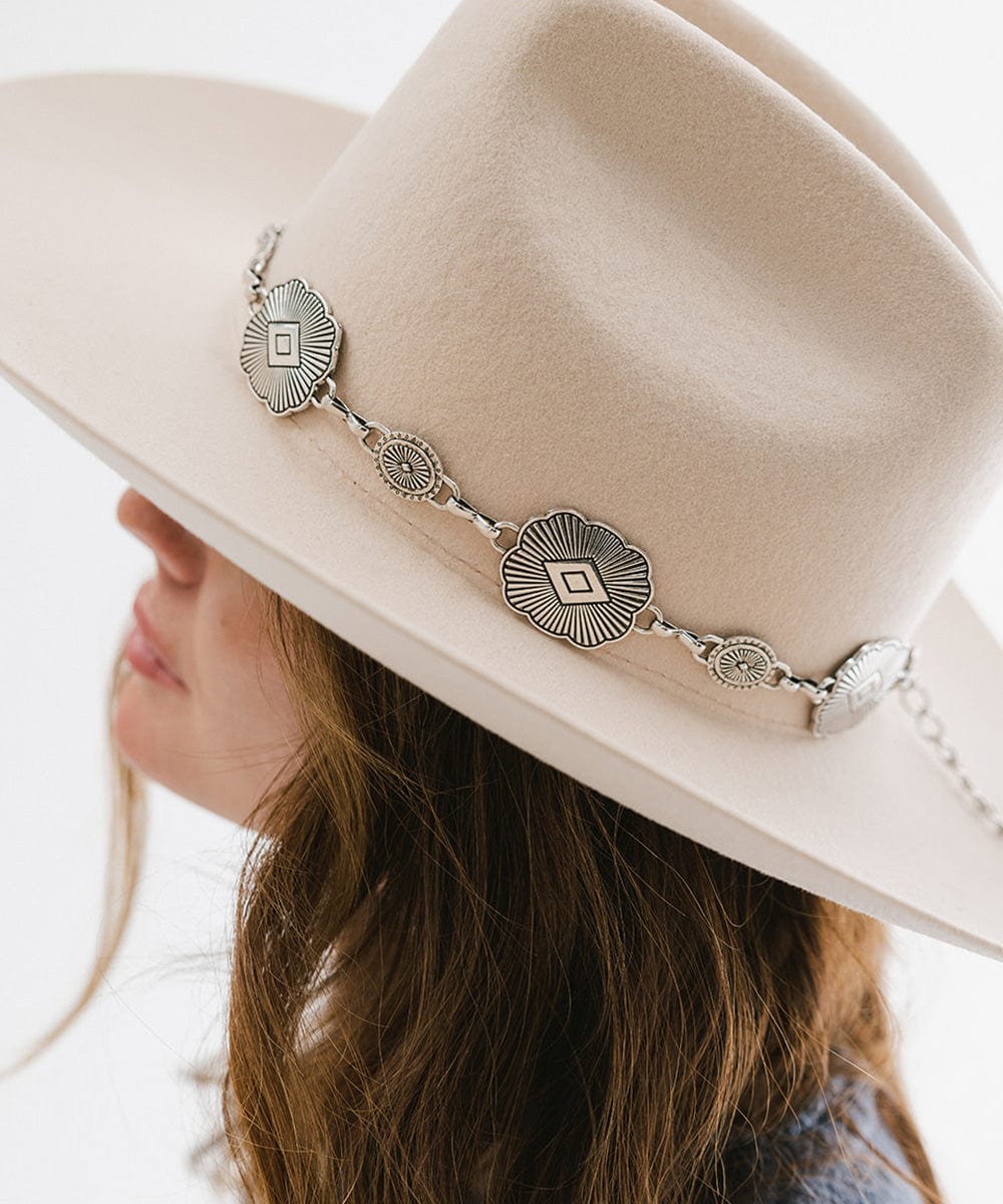 Woman wearing a cream hat with a silver western concho band, facing sideways against a plain background #color_silver