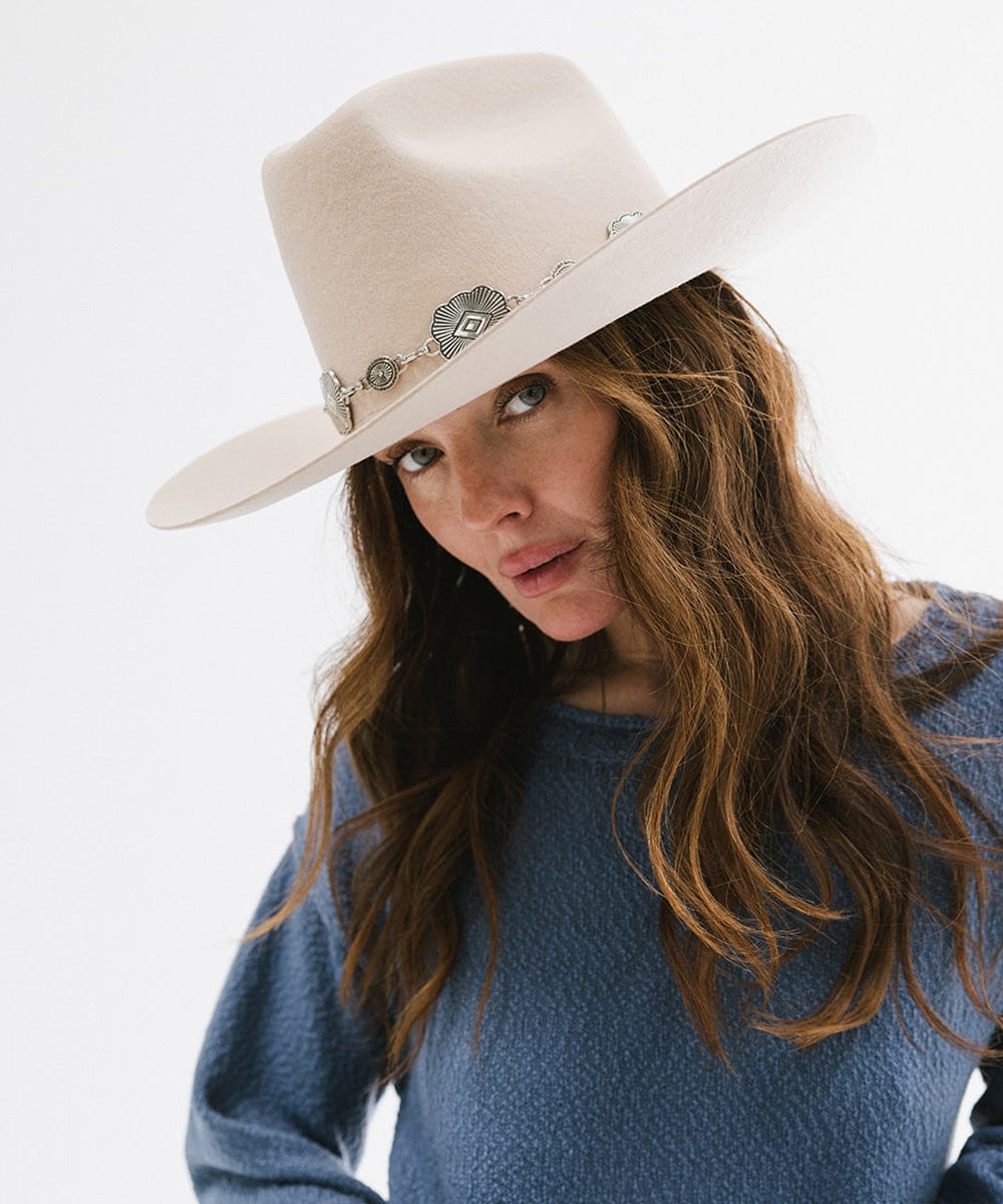 Woman wearing a cream hat with a silver western concho band and a blue sweatshirt against a plain background #color_silver