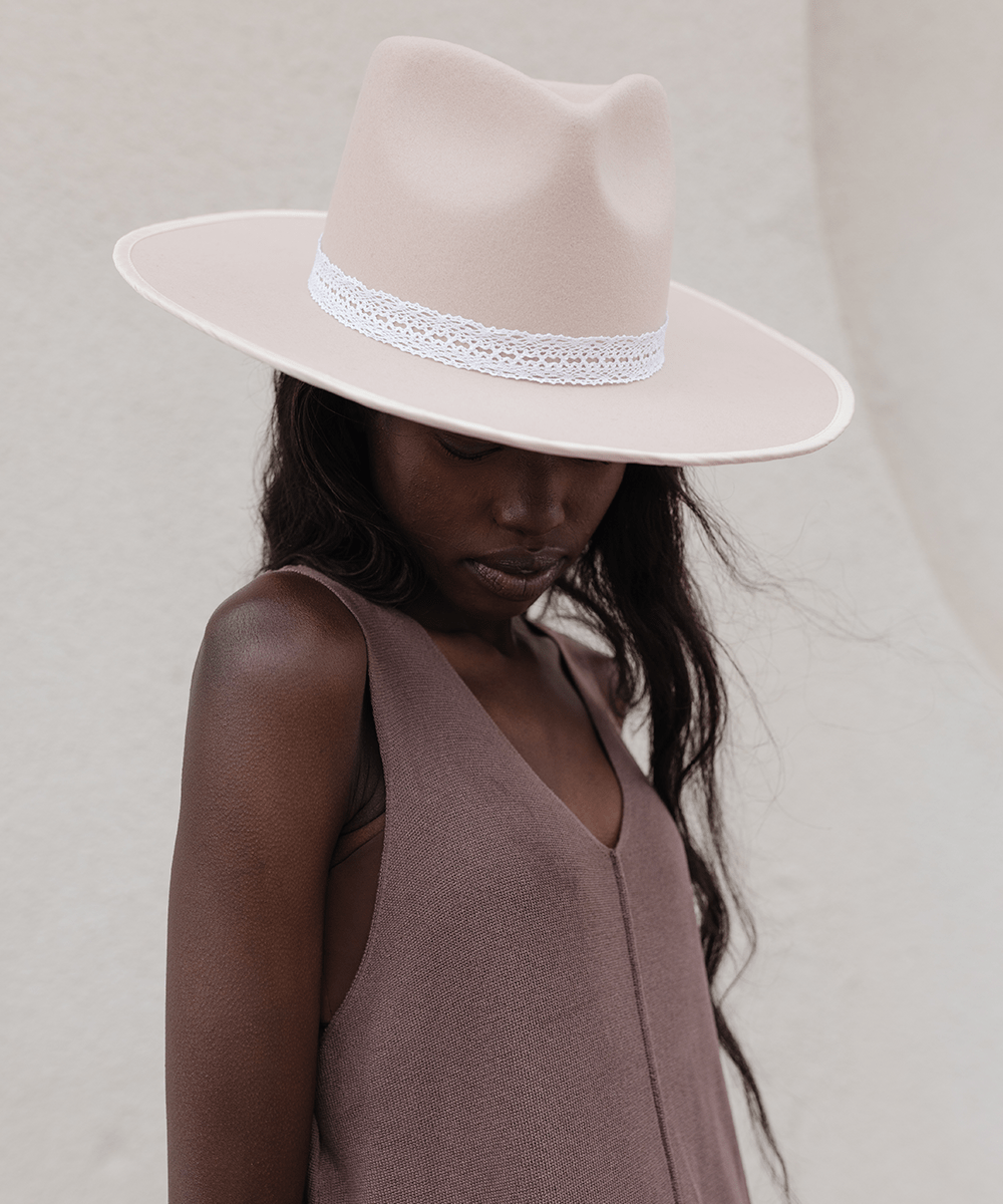 Woman wearing a cream hat with a white lace band and a brown top, looking down against a plain background #color_white