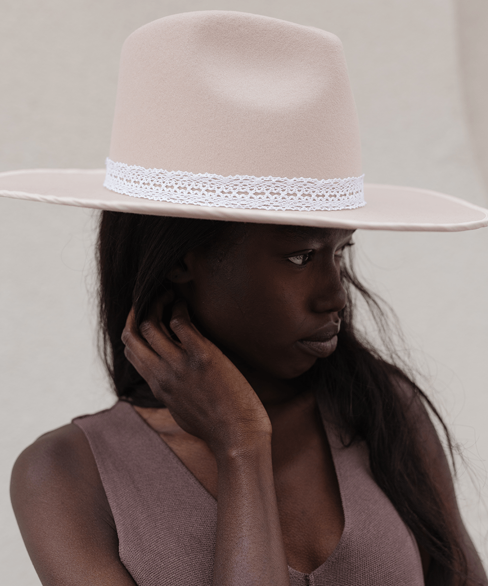 Woman wearing a cream hat with a white lace band and a brown top, looking sideways against a plain background #color_white