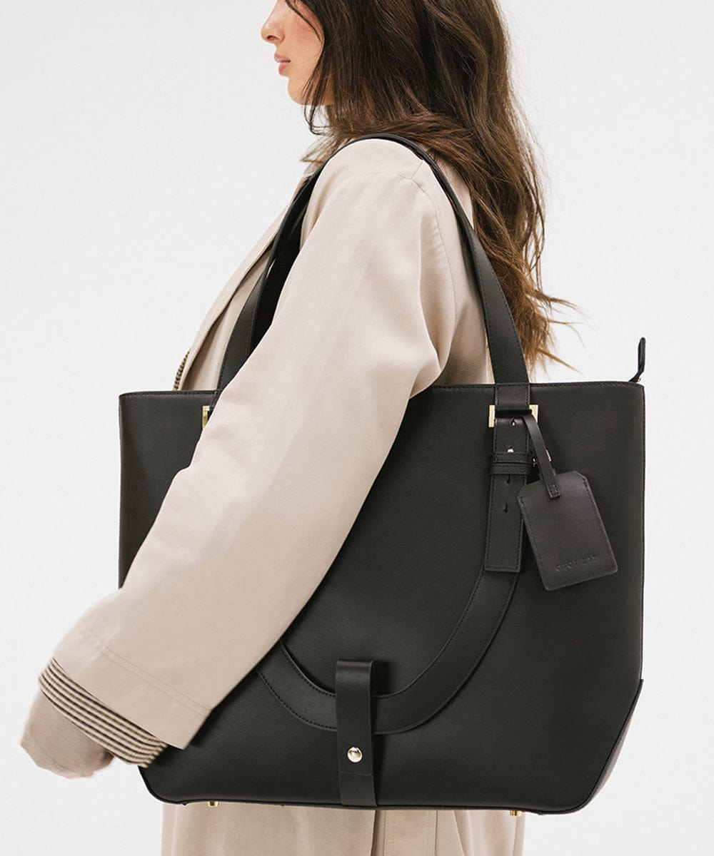 Woman carrying a black Hayes Hat Carrying Tote bag against a plain background #color_black