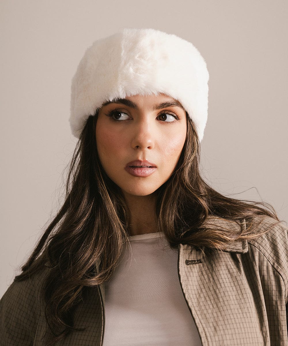 Woman wearing a white fur-lined hat against a neutral background #color_winter white
