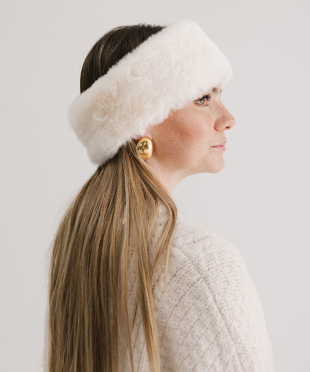 Woman wearing a winter white colored fur headband and a white sweater, facing sideways against a plain background #color_winter white
