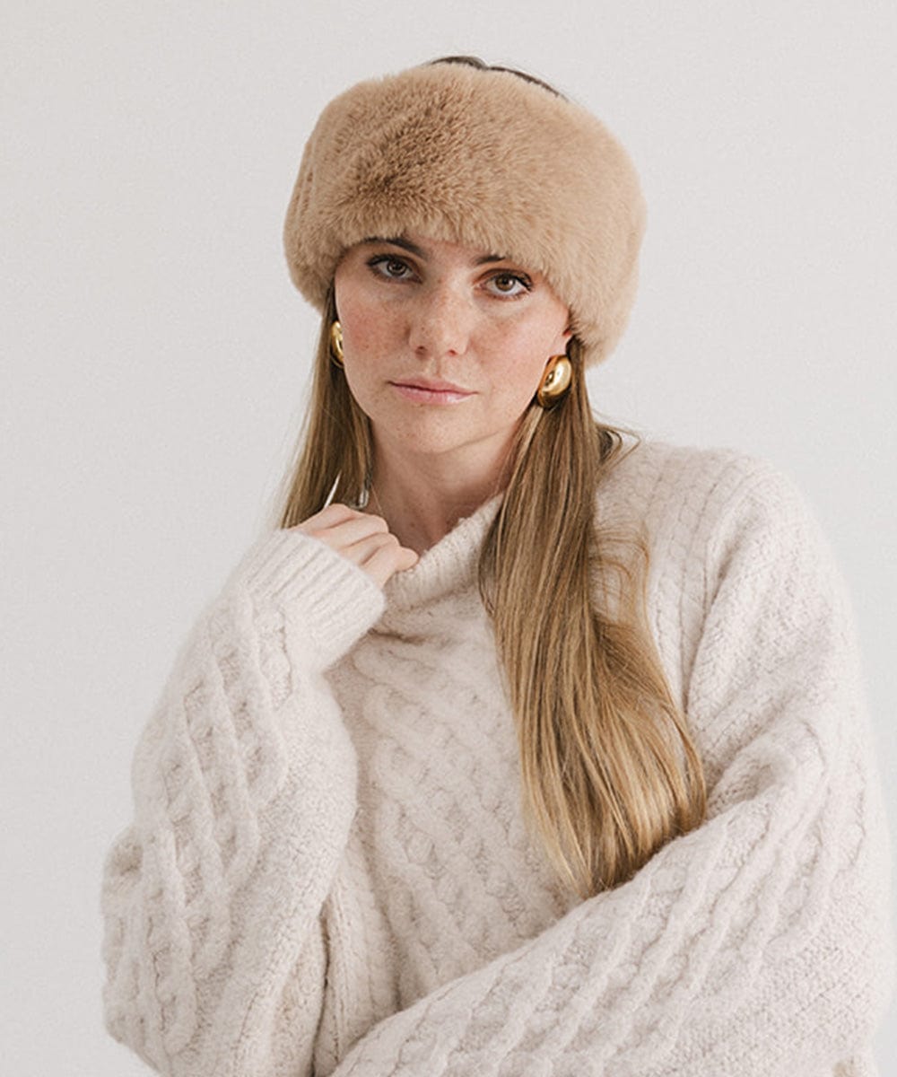 Woman wearing a tan fur headband and a white sweater against a plain background #color_tan