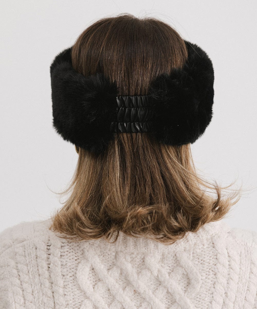 Woman wearing a black fur headband and a white sweater, facing behind against a plain background #color_black
