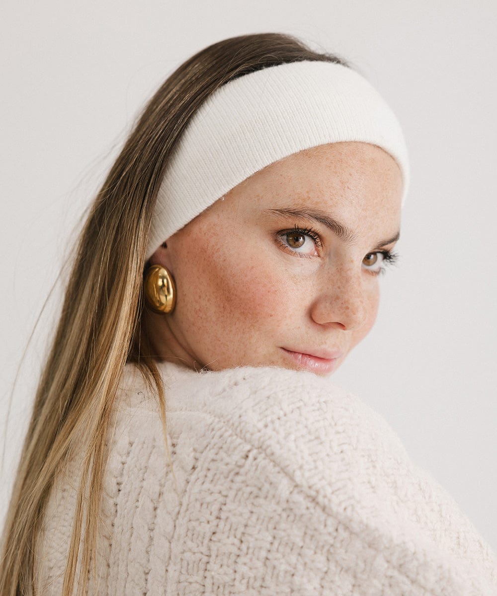 Woman wearing an ivory colored headband and a white sweater, posing sideways against a plain background #color_ivory