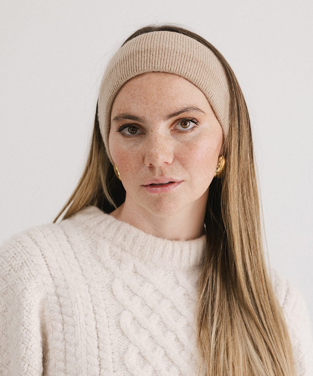 Close up image of a woman wearing a tan headband and a white sweater against a plain background #color_tan