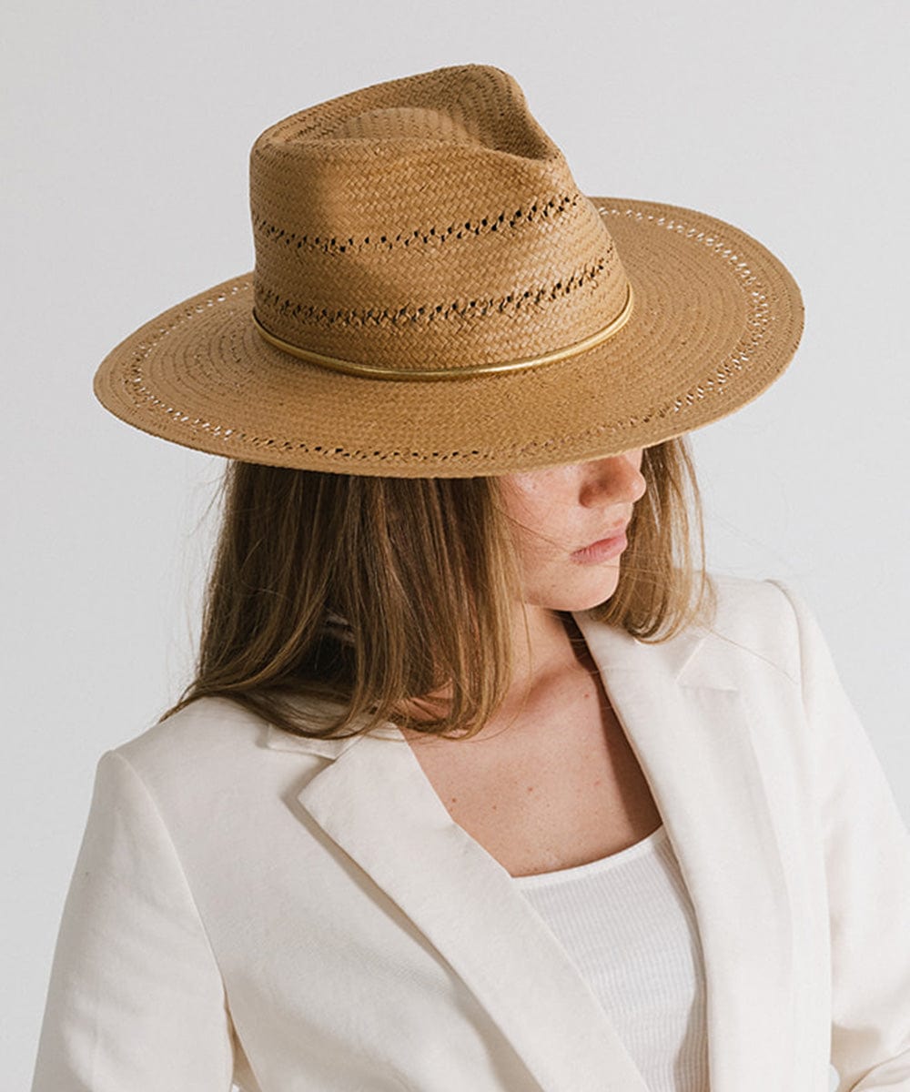 Woman wearing a brown hat with a gold chain hat band and a white blazer against a plain background #color_gold