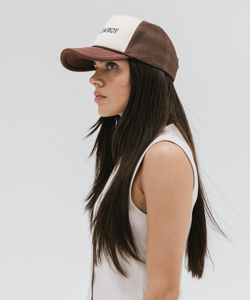 Woman wearing a cream and chocolate brown cap and a white top, facing sideways against a plain background #color_cream-chocolate brown