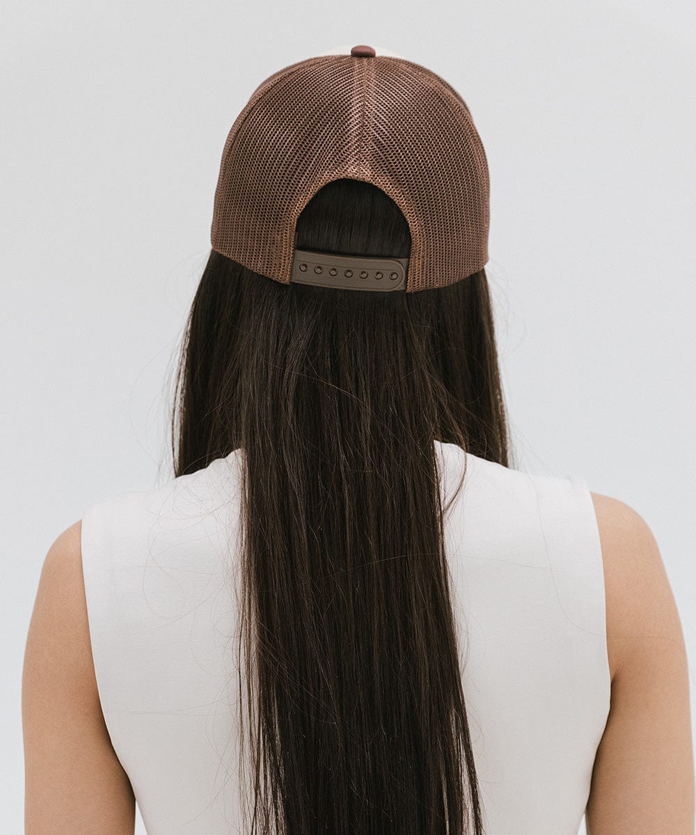 Woman with long hair wearing a cream and chocolate brown cap and a white top against a plain background #color_cream-chocolate brown