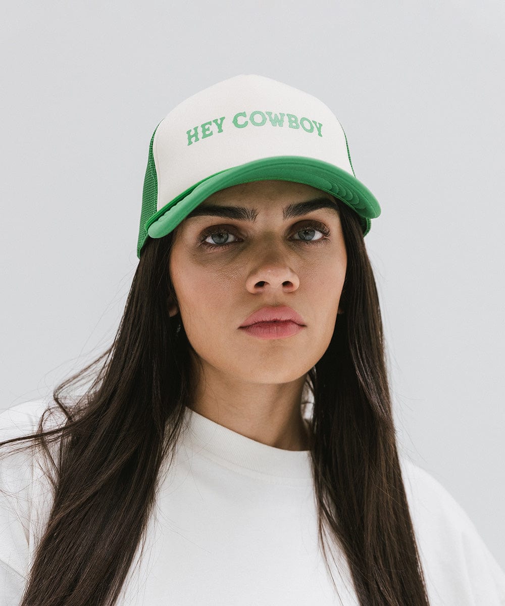 Woman wearing a cream and vintage green cap with 'Hey Cowboy' text and a white t-shirt against a plain background #color_cream-vintage green
