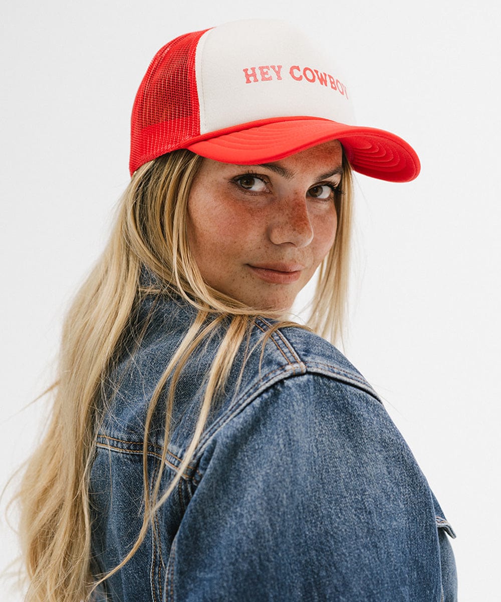 Woman wearing a cream and vintage red cap with 'Hey Cowboy' text and a denim shirt, posing sideways against a plain background #color_cream-vintage red