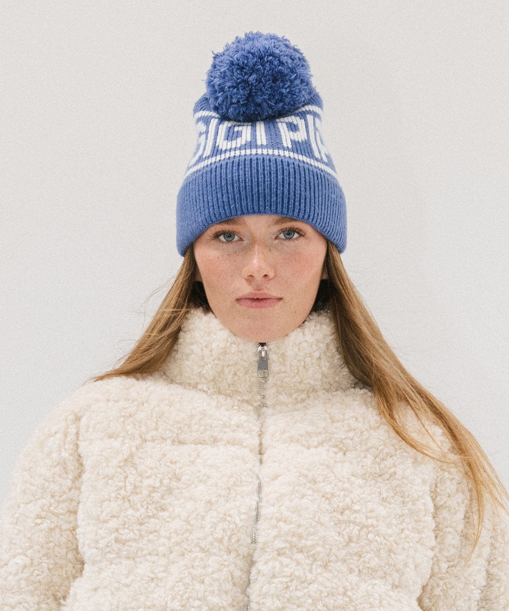 Woman wearing an arctic blue colored knit beanie with pom-pom and 'GIGI PIP' branding and a white sweater against a plain background #color_arctic blue
