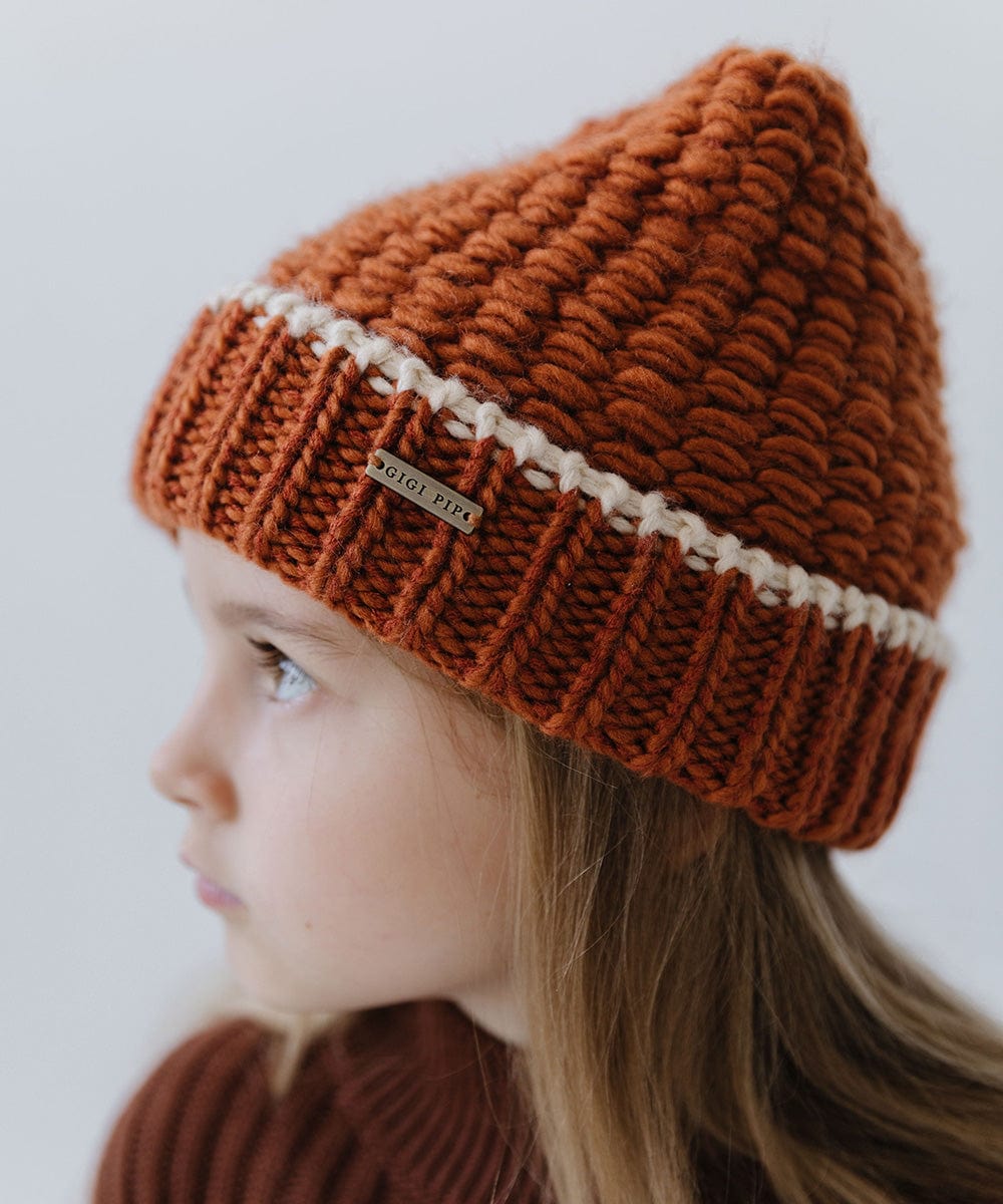 Child wearing a burnt orange vail beanie with a cream stripe looking sideways against a plain background #color_burnt orange-cream