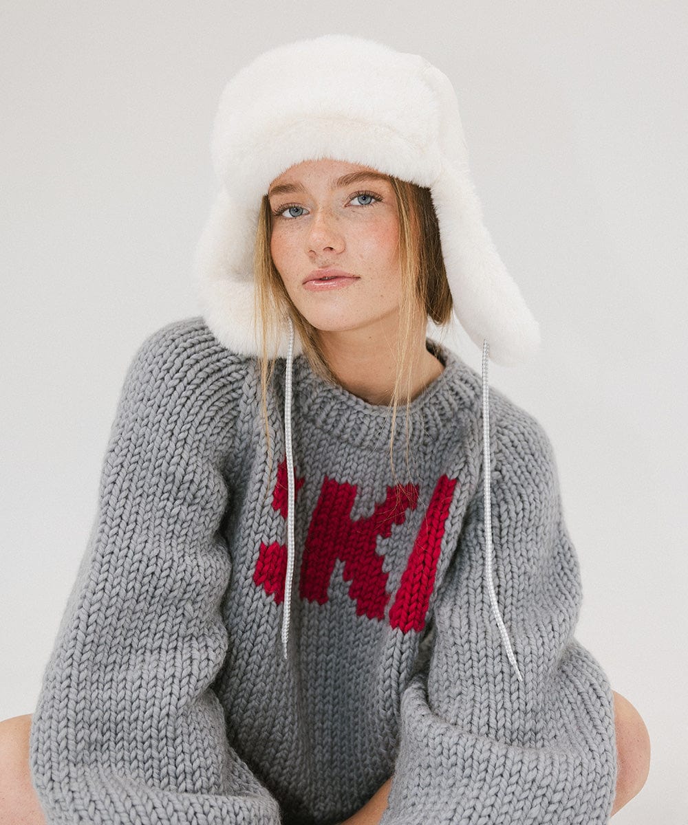 Woman wearing a winter white colored fur-trimmed hat and a grey sweater against a plain background #color_winter white