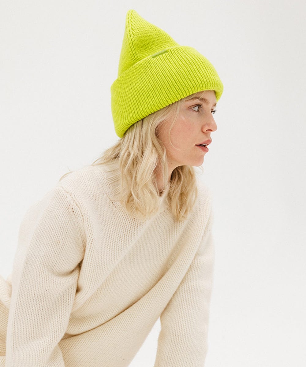 Woman wearing a lime colored oversized knit beanie and a white sweater, facing sideways against a plain background #color_limeade