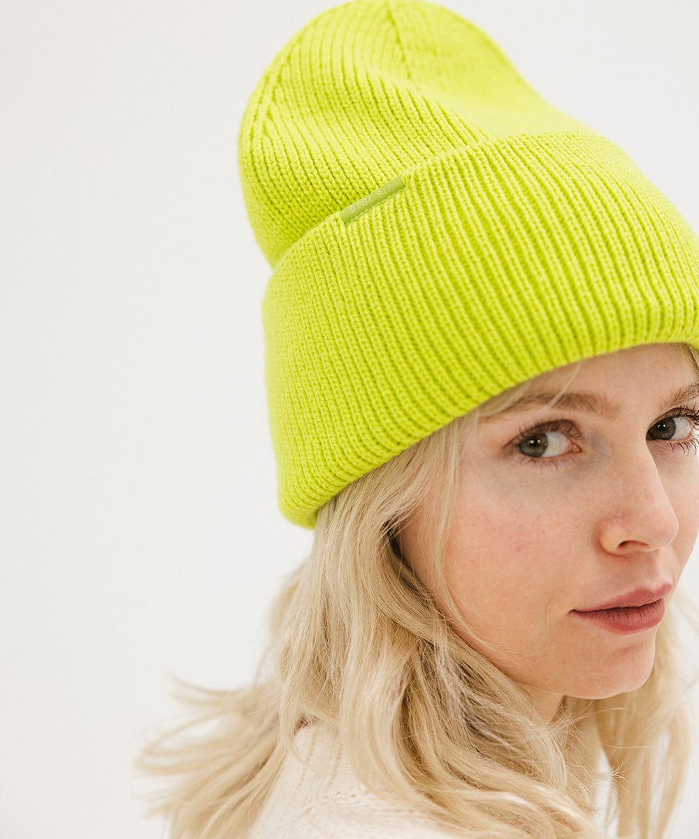 Woman wearing a lime colored oversized knit beanie against a plain background #color_limeade