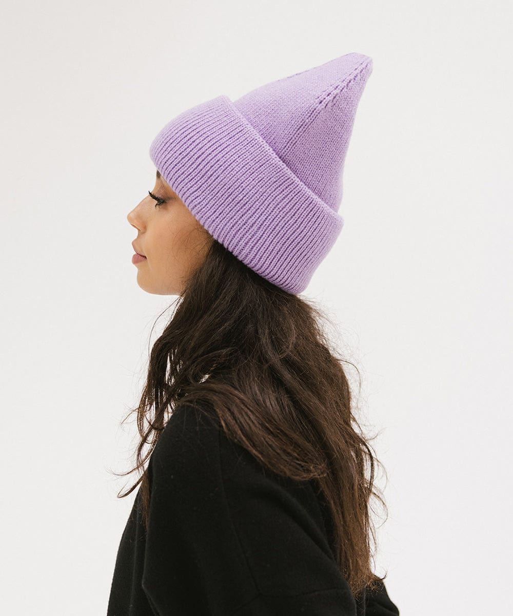 Woman wearing a lavender colored oversized knit beanie and a black t-shirt, facing sideways against a plain background #color_lavender