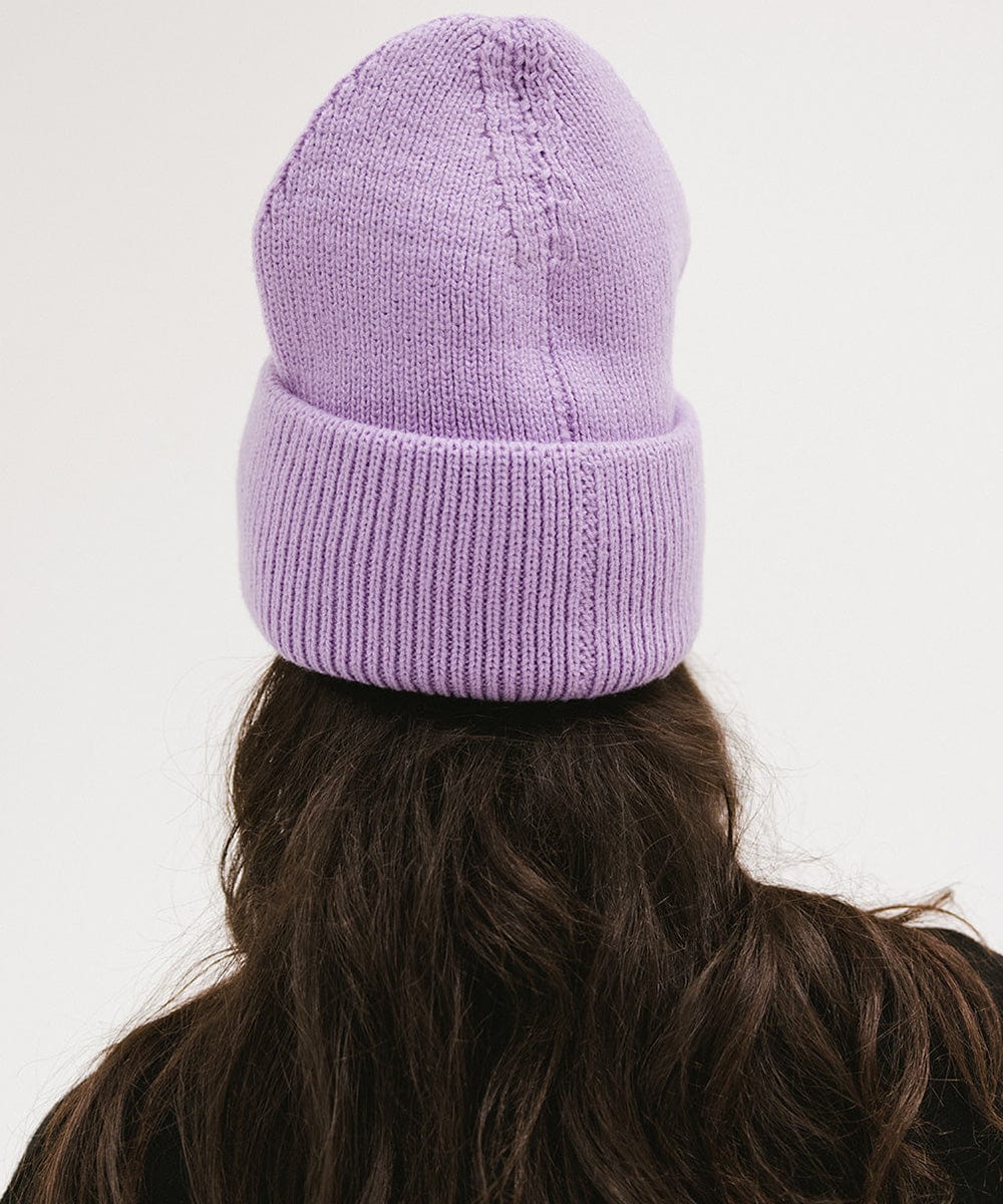 Person with long hair wearing a lavender colored oversized knit beanie against a plain background #color_lavender