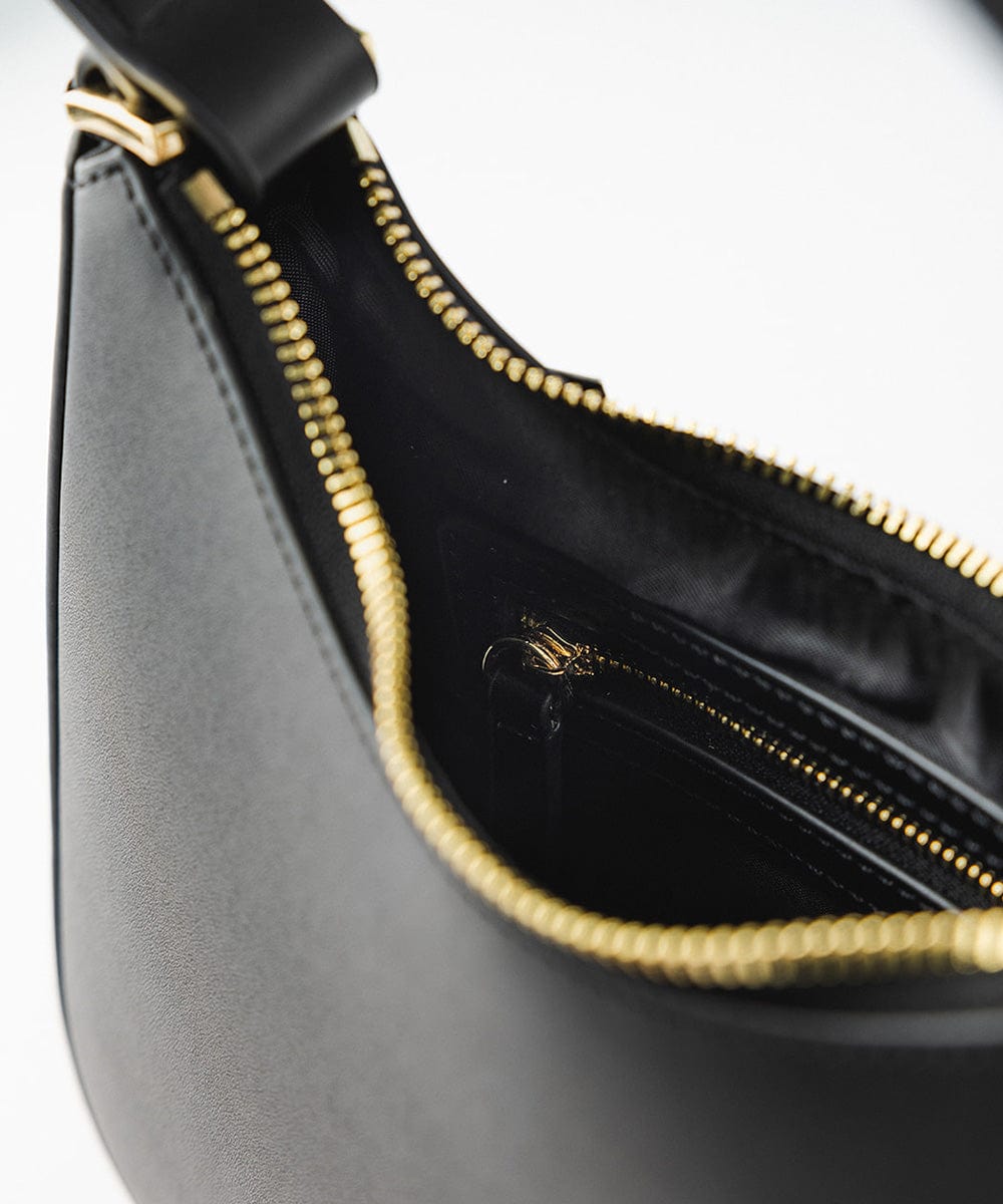 A black genuine leather handbag with a golden zipper against a plain background #color_black