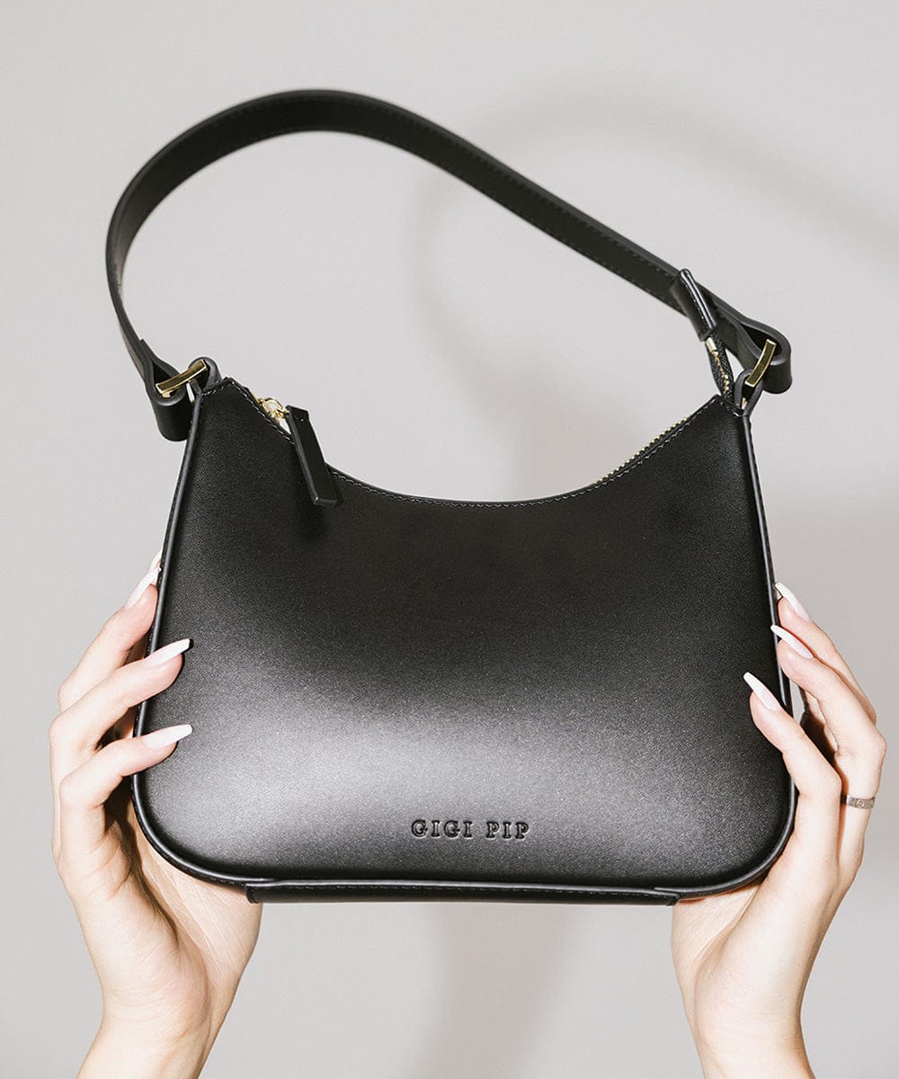 A black genuine leather handbag with a shoulder strap being held by someone against a plain background #color_black