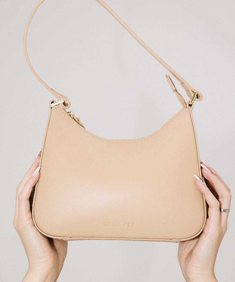 A tan genuine leather handbag being held by someone on a plain background #color_tan