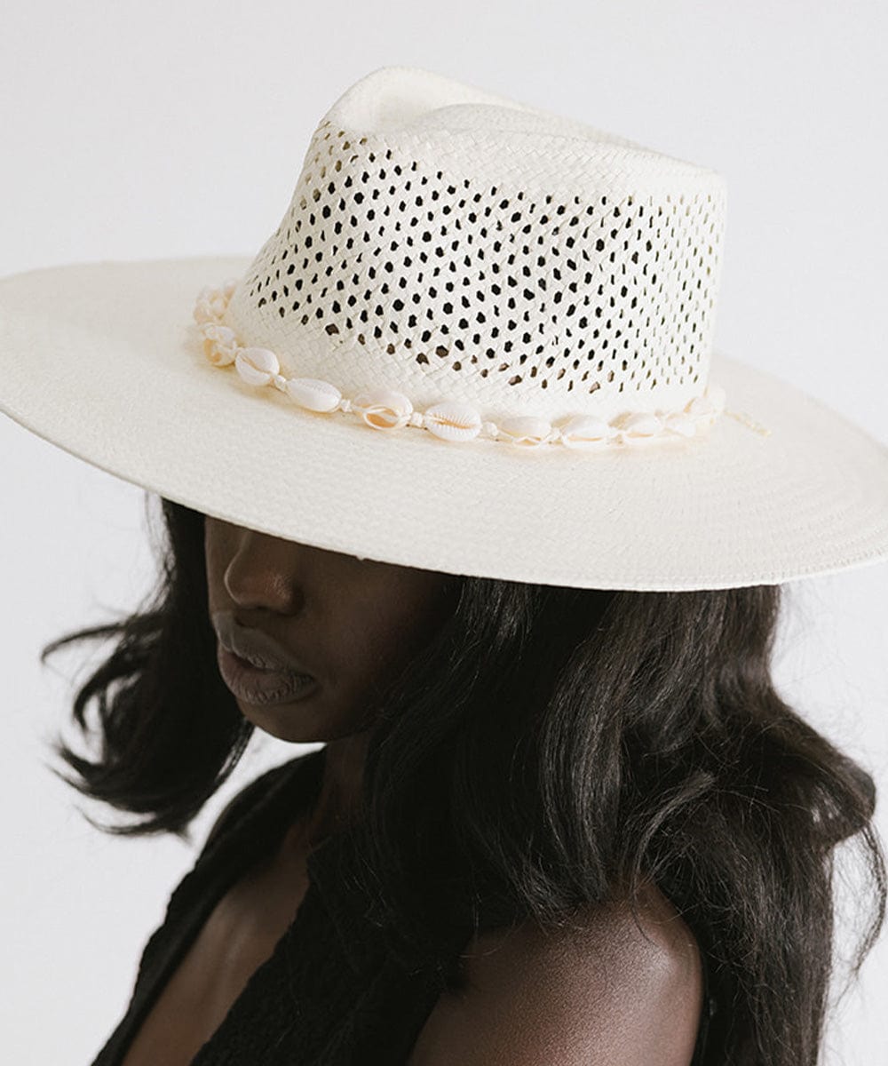 Woman wearing a white hat with a white shell hat band and a black top, facing sideways against a plain background #color_natural