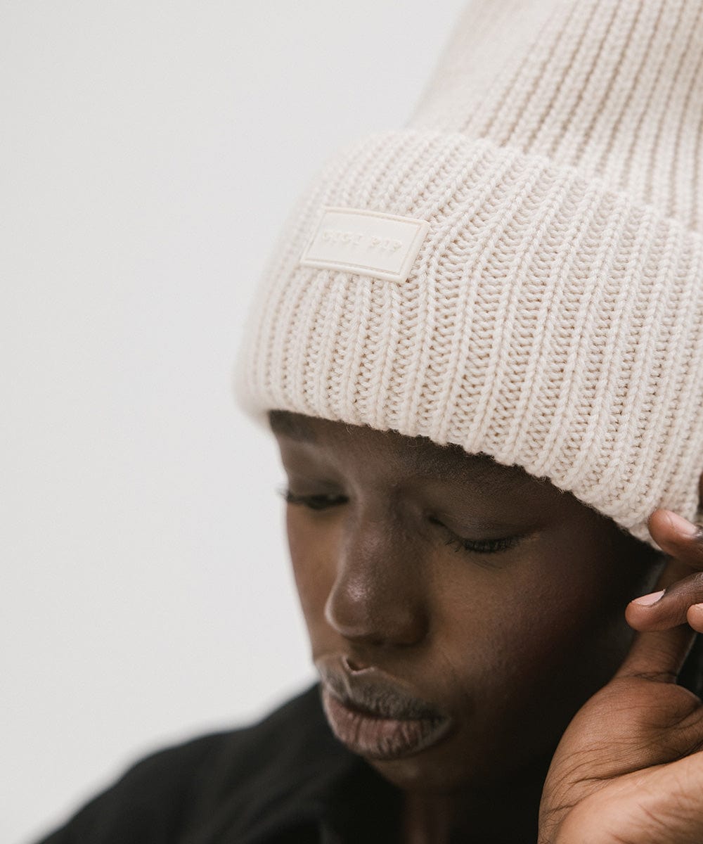A person wearing an off white colored ribbed beanie against a plain background #color_off white