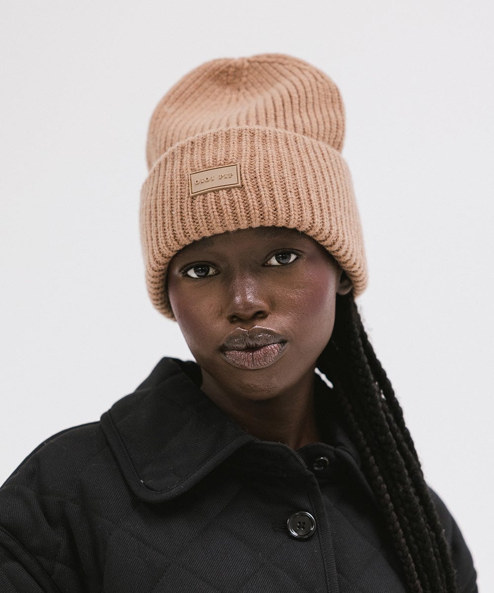 A woman wearing a brown colored ribbed beanie and a black jacket against a plain background #color_brown
