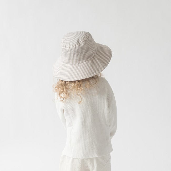 Young girl wearing a latte colored bucket hat and a white shirt, facing behind against a plain background #color_latte