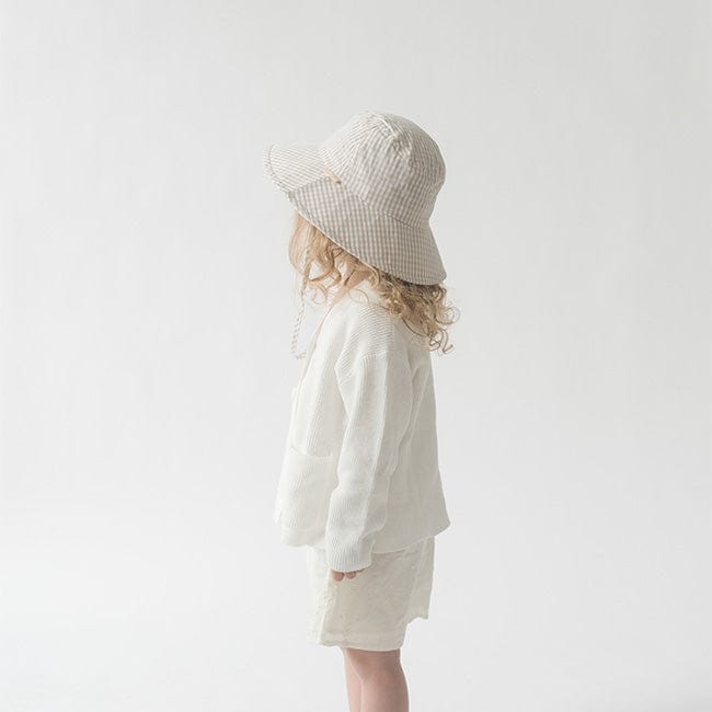 Young girl wearing a latte colored bucket hat, a white shirt and white shorts, facing sideways against a plain background #color_latte