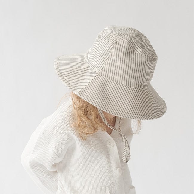 Young girl wearing a grey striped bucket hat and a white shirt, looking down against a plain background #color_grey