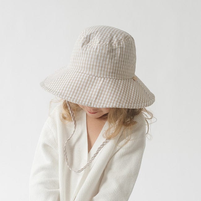 Young girl wearing a latte colored bucket hat and a white shirt, looking down against a plain background #color_latte