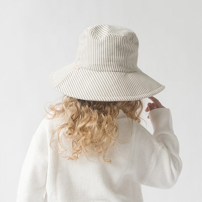 Young girl wearing a grey striped bucket hat and a white shirt, facing behind against a plain background #color_grey