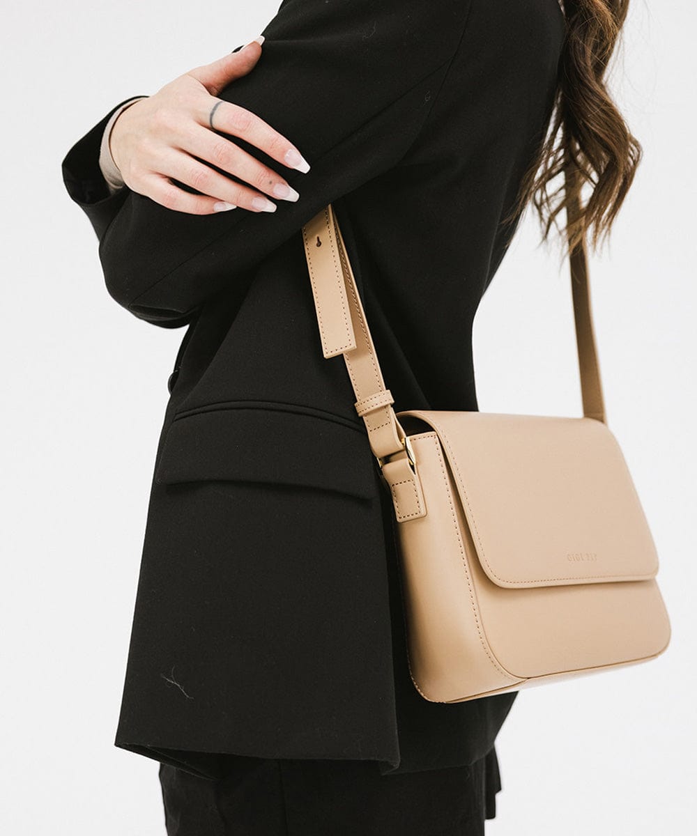 Person wearing a black coat carrying a tan Rhys Crossbody Genuine Leather Bag, posing sideways against a plain background #color_tan