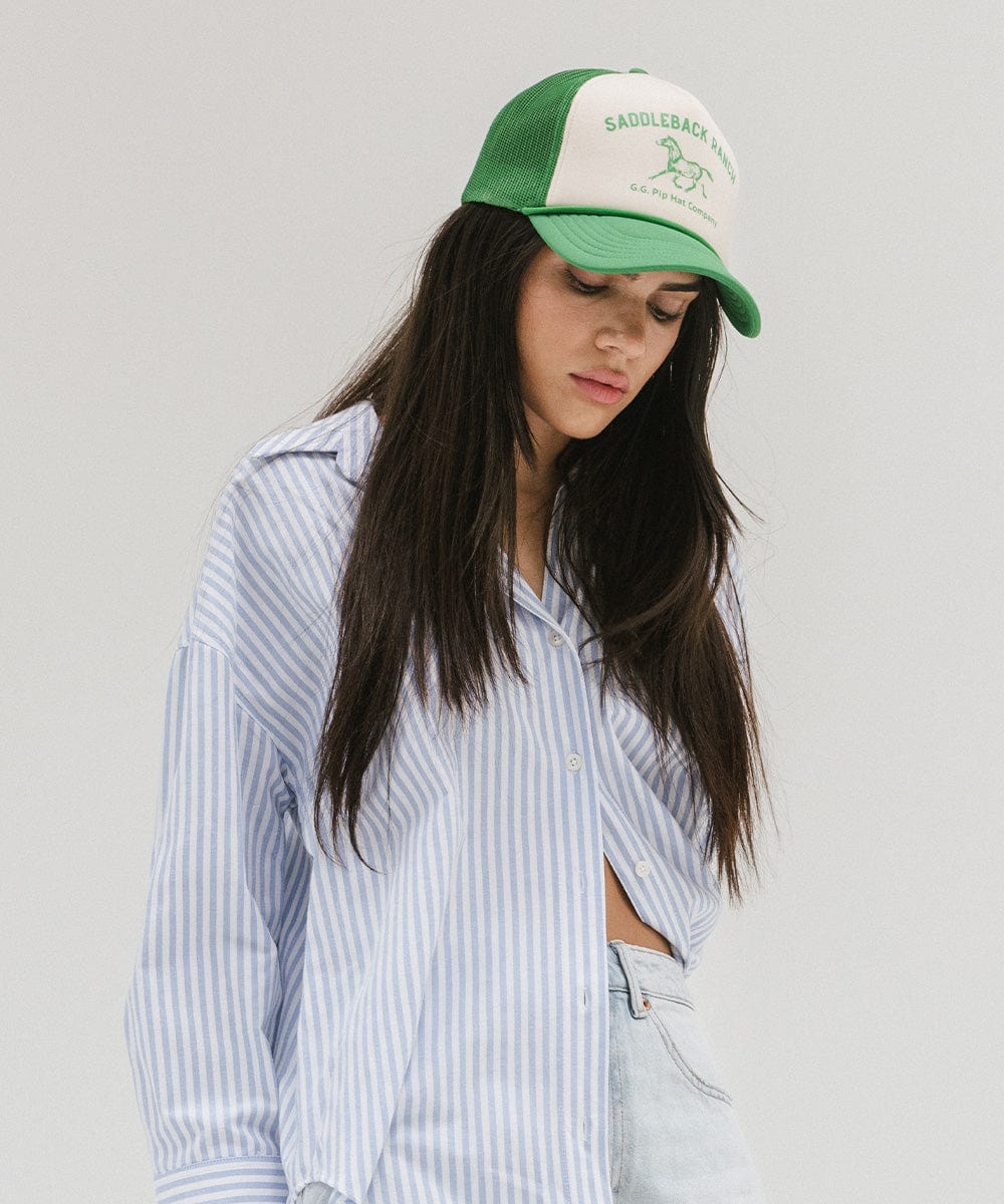Woman wearing a cream and vintage green cap with 'Saddleback Ranch' text and logo, and a shirt, posing against a plain background #color_cream - vintage green