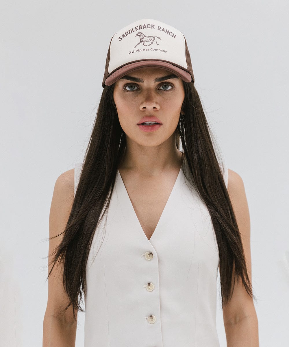 Woman wearing a cream and chocolate brown cap with 'Saddleback Ranch' text and logo, and a white top against a plain background #color_cream - chocolate brown