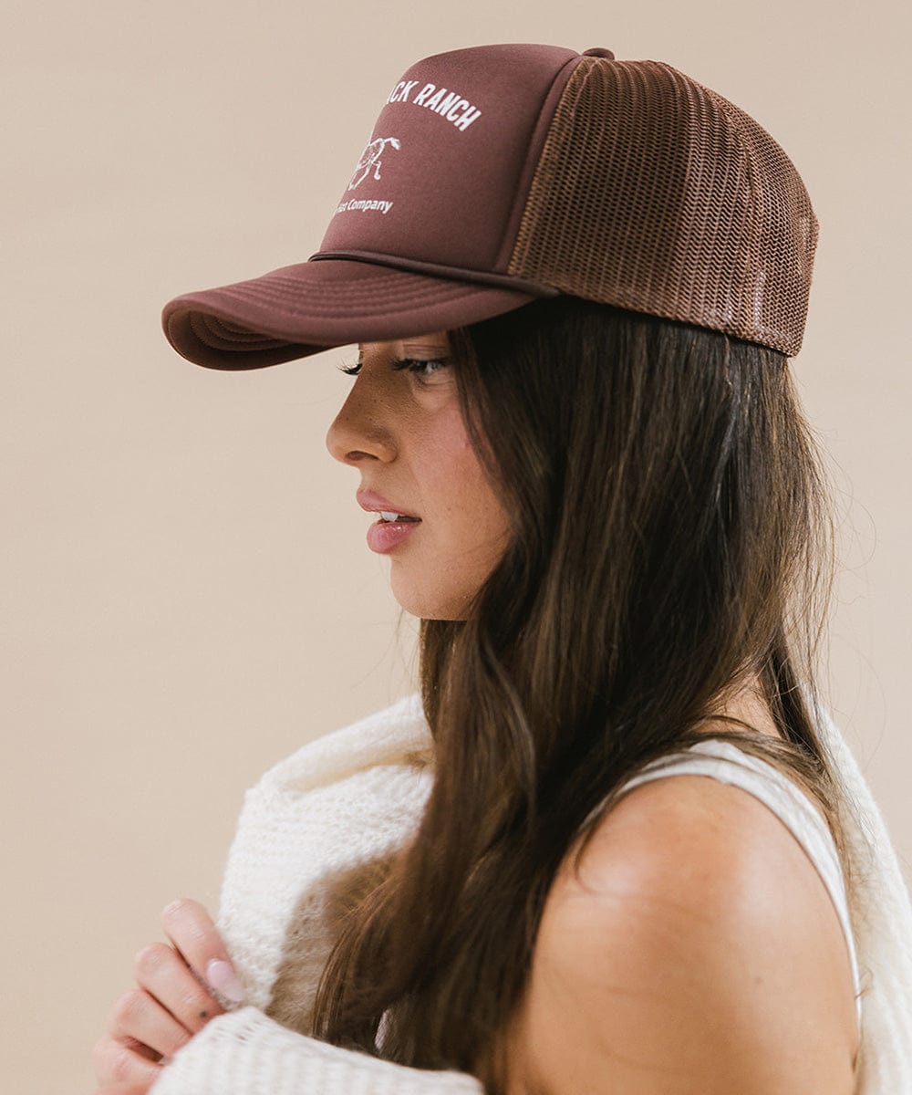 Woman wearing chocolate brown cap and a white top, facing sideways against a plain background #color_chocolate brown