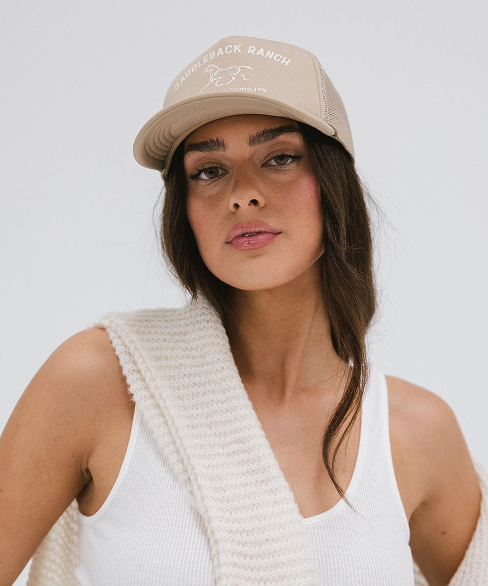 Woman wearing a tan cap with 'Saddleback Ranch' text and logo, and a white top against a plain background #color_tan