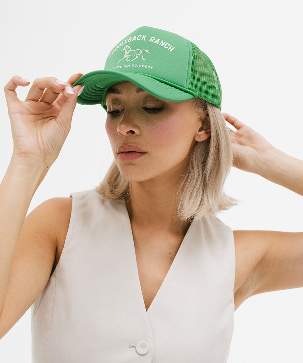Woman wearing a vintage green colored cap with 'Saddleback Ranch' text and logo, and a white top against a plain background #color_vintage green