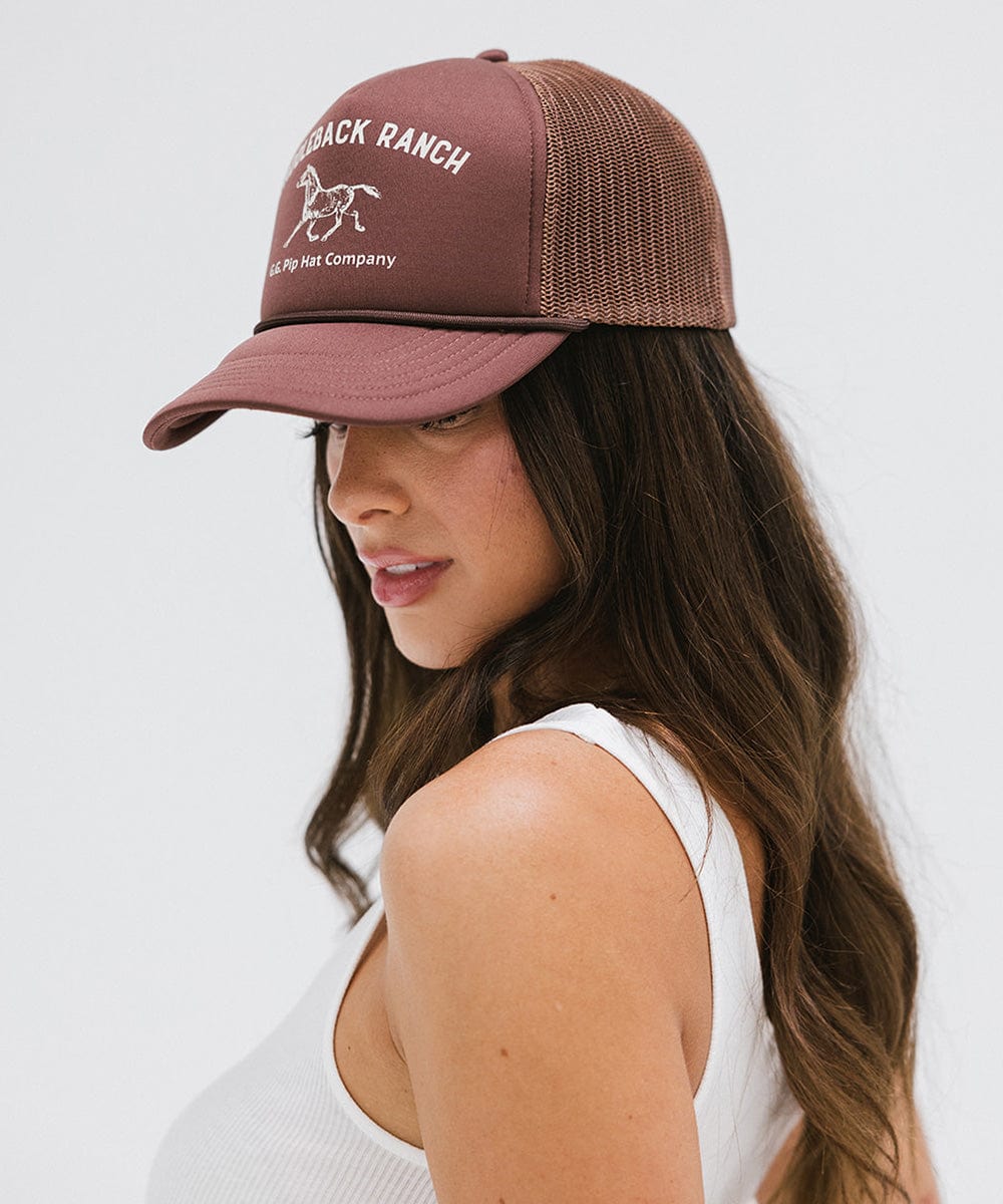 Woman wearing chocolate brown cap with 'Saddleback Ranch' text and logo, and a white top, posing sideways against a plain background #color_chocolate brown