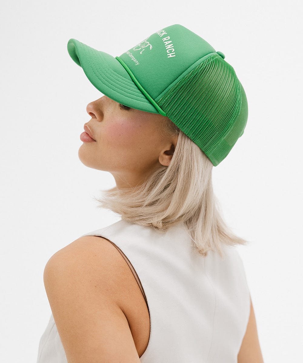 Woman wearing a vintage green colored cap with 'Saddleback Ranch' text and logo, and a white top, facing sideways against a plain background #color_vintage green
