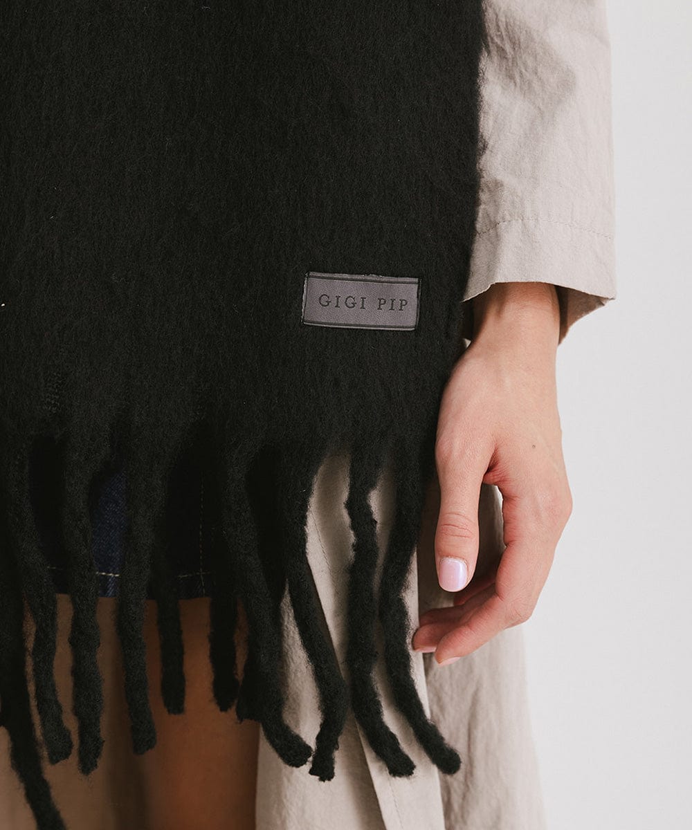 A black oversized knit scarf with fringes worn by a person against a plain background #color_black