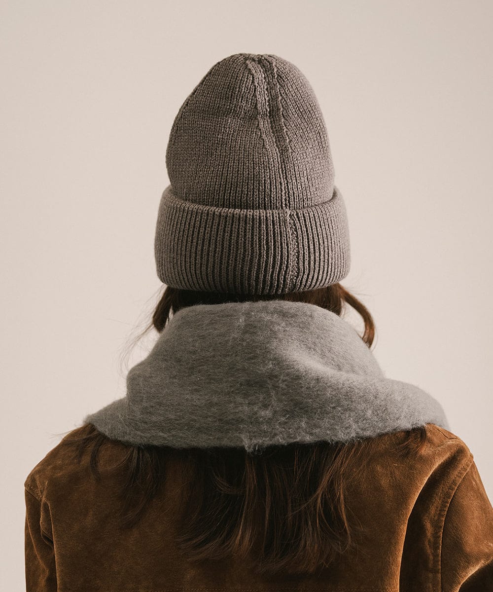 Person wearing a gray knit beanie and scarf with a brown jacket on a plain background #color_grey
