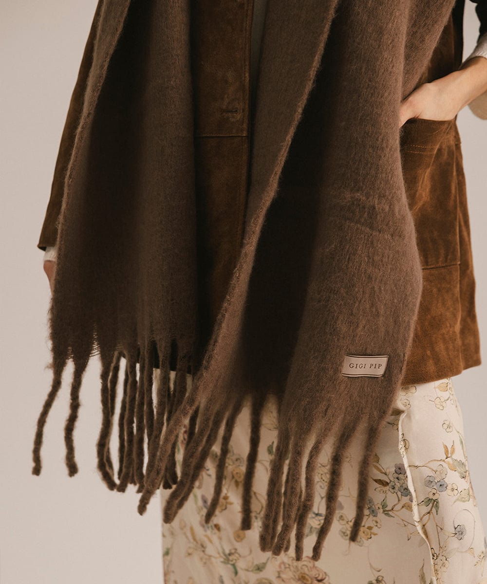 Brown scarf with fringe and brand label draped over a person wearing a floral dress. #color_brown