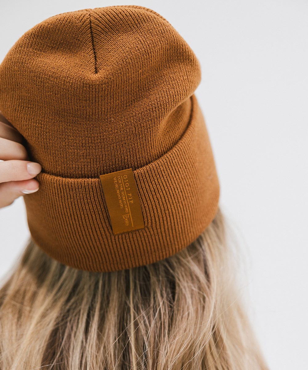 Close up image of someone wearing a cocoa colored beanie with the brand label against a plain background #color_cocoa