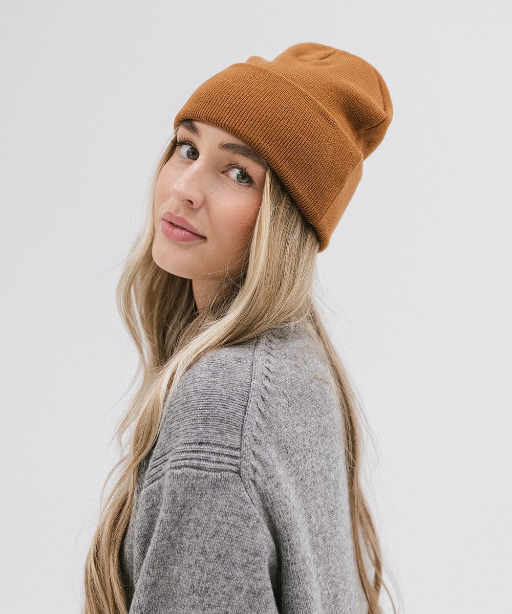 Woman wearing a cocoa colored beanie and a grey sweater, posing sideways against a plain background #color_cocoa