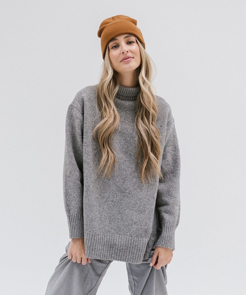 Woman wearing a cocoa colored beanie, a grey sweater and grey pants against a plain background #color_cocoa