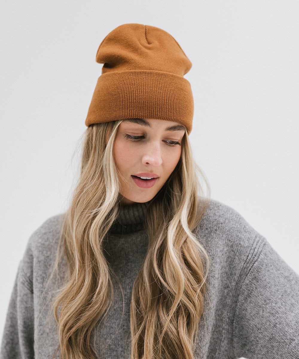 Woman wearing a cocoa colored beanie and a grey sweater, posing against a plain background #color_cocoa